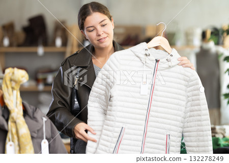 Positive young girl choosing down jacket in clothing store Positive young girl choosing down jacket in clothing store 132278249