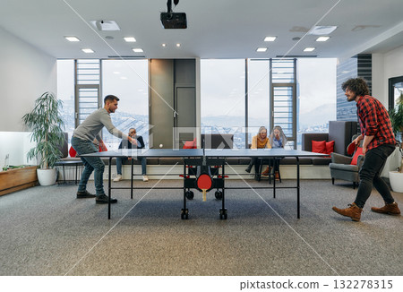 Business colleagues take a break from work to enjoy a game of table tennis, fostering teamwork and camaraderie in the workplace 132278315