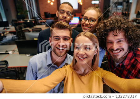 A diverse group of business professionals take a break from their tasks in a modern startup office to capture a creative selfie, showcasing teamwork and a vibrant workplace culture 132278317