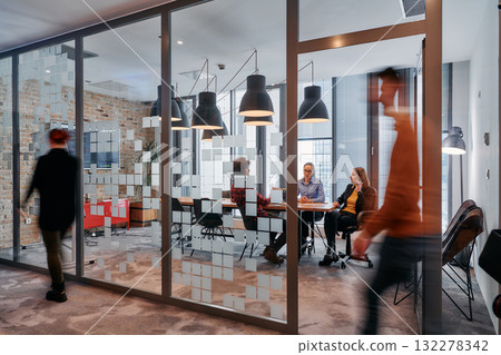 In the dynamic hustle and bustle of a business environment, a group of young business professionals walk down the corridor next to their office, while their colleagues collaborate inside, symbolizing In the dynamic hustle and bustle of a business environment, a group of young business professionals walk down the corridor next to their office, while their colleagues collaborate inside, symbolizing 132278342