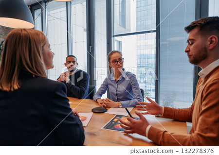 In the vibrant ambiance of a modern startup office, a diverse team of business professionals engage in discussions on various projects and develop new business strategies, epitomizing creativity and 132278376