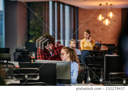 Business colleagues, a man and a woman, engage in discussing business strategies while attentively gazing at a computer monitor, epitomizing collaboration and innovation 132278437