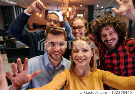 A diverse group of business professionals take a break from their tasks in a modern startup office to capture a creative selfie, showcasing teamwork and a vibrant workplace culture 132278440