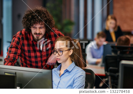 Business colleagues, a man and a woman, engage in discussing business strategies while attentively gazing at a computer monitor, epitomizing collaboration and innovation Business colleagues, a man and a woman, engage in discussing business strategies while attentively gazing at a computer monitor, epitomizing collaboration and innovation 132278458