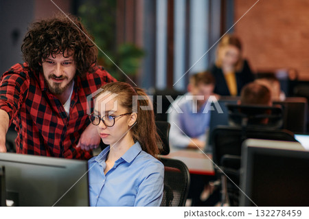 Business colleagues, a man and a woman, engage in discussing business strategies while attentively gazing at a computer monitor, epitomizing collaboration and innovation 132278459