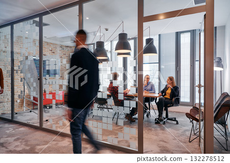 In the dynamic hustle and bustle of a business environment, a group of young business professionals walk down the corridor next to their office, while their colleagues collaborate inside, symbolizing In the dynamic hustle and bustle of a business environment, a group of young business professionals walk down the corridor next to their office, while their colleagues collaborate inside, symbolizing 132278512
