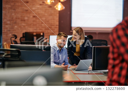 Business colleagues, a man and a woman, engage in discussing business strategies while attentively gazing at a computer monitor, epitomizing collaboration and innovation Business colleagues, a man and a woman, engage in discussing business strategies while attentively gazing at a computer monitor, epitomizing collaboration and innovation 132278600