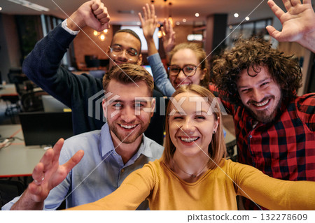 A diverse group of business professionals take a break from their tasks in a modern startup office to capture a creative selfie, showcasing teamwork and a vibrant workplace culture 132278609