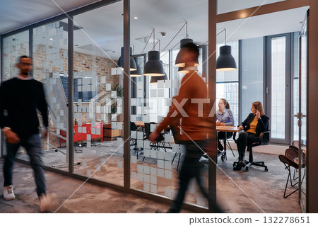 In the dynamic hustle and bustle of a business environment, a group of young business professionals walk down the corridor next to their office, while their colleagues collaborate inside, symbolizing In the dynamic hustle and bustle of a business environment, a group of young business professionals walk down the corridor next to their office, while their colleagues collaborate inside, symbolizing 132278651