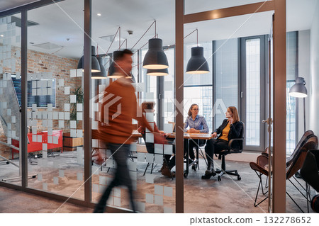 In the dynamic hustle and bustle of a business environment, a group of young business professionals walk down the corridor next to their office, while their colleagues collaborate inside, symbolizing In the dynamic hustle and bustle of a business environment, a group of young business professionals walk down the corridor next to their office, while their colleagues collaborate inside, symbolizing 132278652