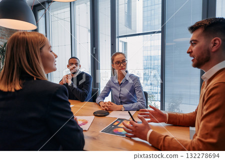 In the vibrant ambiance of a modern startup office, a diverse team of business professionals engage in discussions on various projects and develop new business strategies, epitomizing creativity and 132278694