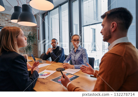 In the vibrant ambiance of a modern startup office, a diverse team of business professionals engage in discussions on various projects and develop new business strategies, epitomizing creativity and 132278714