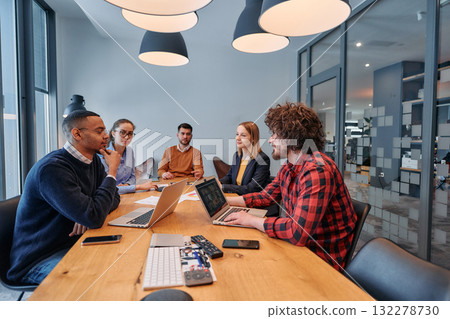 In the vibrant ambiance of a modern startup office, a diverse team of business professionals engage in discussions on various projects and develop new business strategies, epitomizing creativity and 132278730