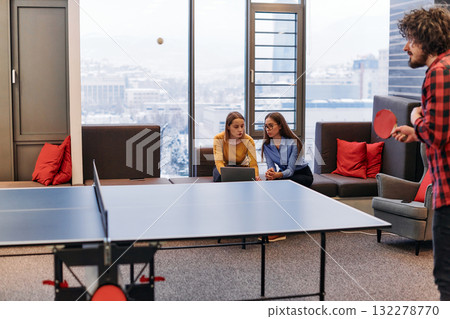 Business colleagues take a break from work to enjoy a game of table tennis, fostering teamwork and camaraderie in the workplace 132278770