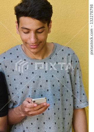 Middle Eastern Teenager Using Mobile Phone While Leaning Against Yellow Wall 132278798