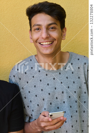 Middle Eastern Teenager Using Mobile Phone While Leaning Against Yellow Wall 132278804