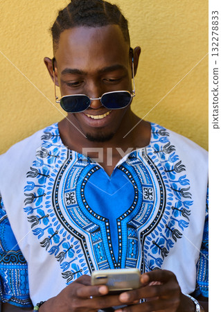 African American Teenager in Traditional Sudanese Attire Engaged with Smartphone African American Teenager in Traditional Sudanese Attire Engaged with Smartphone 132278833