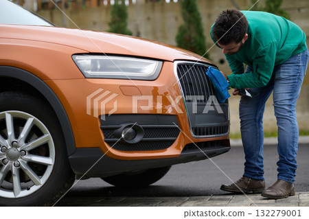 A man meticulously washes and cleans his car in the driveway of his home, showcasing pride in his vehicle and outdoor space. A man meticulously washes and cleans his car in the driveway of his home, showcasing pride in his vehicle and outdoor space. 132279001