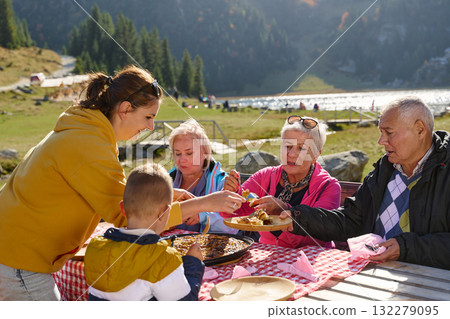 A family on a mountain vacation indulges in the pleasures of a healthy life, savoring traditional pie while surrounded by the breathtaking beauty of nature, fostering family bonds and embracing the 132279095