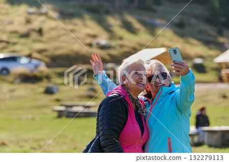 An elderly pair of women captures a timeless moment on their smartphones, blending technology with the serene beauty that surrounds them 132279113