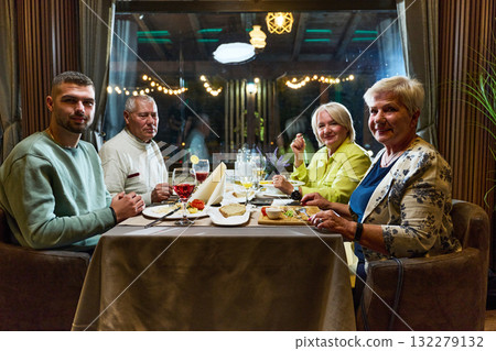 A group of family friends, comprising a young grandson and older individuals, share a delightful dinner in a modern restaurant, exemplifying the concept of healthy aging through intergenerational 132279132