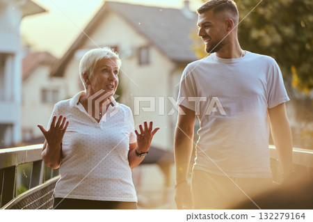 A handsome man and an older woman share a serene walk in nature, crossing a beautiful bridge against the backdrop of a stunning sunset, embodying the concept of a healthy and vibrant intergenerational A handsome man and an older woman share a serene walk in nature, crossing a beautiful bridge against the backdrop of a stunning sunset, embodying the concept of a healthy and vibrant intergenerational 132279164