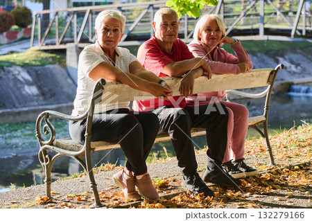 A group of elderly individuals, including a senior man and two older women, sits in a park on a sunny autumn day, embodying the concept of healthy aging through companionship, relaxation, and outdoor A group of elderly individuals, including a senior man and two older women, sits in a park on a sunny autumn day, embodying the concept of healthy aging through companionship, relaxation, and outdoor 132279166