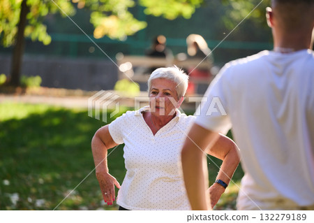 A group of seniors follows a trainer, engaging in outdoor exercises in the park, as they collectively strive to maintain vitality and well-being, embracing an active and health-conscious lifestyle in A group of seniors follows a trainer, engaging in outdoor exercises in the park, as they collectively strive to maintain vitality and well-being, embracing an active and health-conscious lifestyle in 132279189