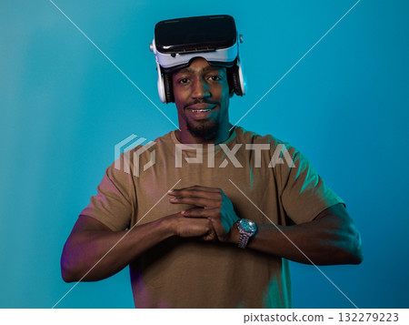 In an avant-garde scene, an African American man engages in cutting-edge virtual reality gaming, utilizing VR glasses to immerse himself in futuristic boxing games, set against a vivid blue background 132279223