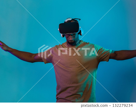 African American man dons VR glasses, engrossed in a virtual reality simulation, gesturing with hands, against a striking blue background, highlighting the fusion of cutting-edge technology and 132279234