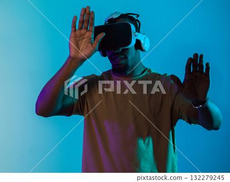 Immersed in a digital realm, an African American man navigates the virtual landscape with a VR goggles, using tactile gestures to interact with virtual objects, showcasing a harmonious blend of 132279245