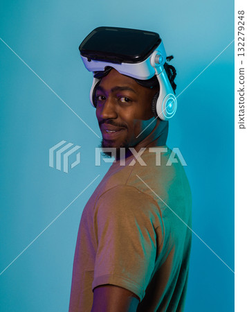 In a futuristic visual, an African American man stands isolated against a striking blue backdrop, adorned with VR glasses that transport him into a cutting-edge virtual reality experience, merging 132279248