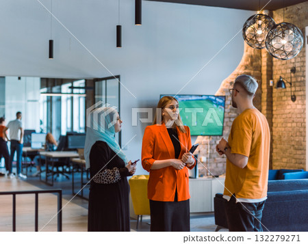 A group of young business colleagues, including a woman in a hijab, stands united in the modern corridor of a spacious startup coworking center, representing diversity and collaborative spirit 132279271