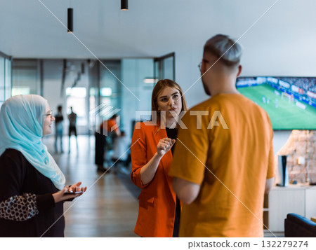 A group of young business colleagues, including a woman in a hijab, stands united in the modern corridor of a spacious startup coworking center, representing diversity and collaborative spirit 132279274