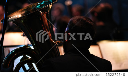 Musician with brass instrument performing in orchestra with dramatic lighting 132279348
