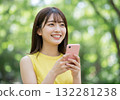 A smiling woman operating a smartphone in the greenery 132281238