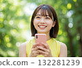 A smiling woman operating a smartphone in the greenery 132281239