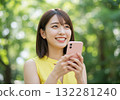 A smiling woman operating a smartphone in the greenery 132281240