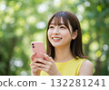 A smiling woman operating a smartphone in the greenery 132281241