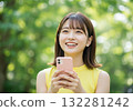 A smiling woman operating a smartphone in the greenery 132281242
