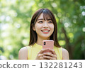 A smiling woman operating a smartphone in the greenery 132281243