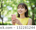 A smiling woman operating a smartphone in the greenery 132281244