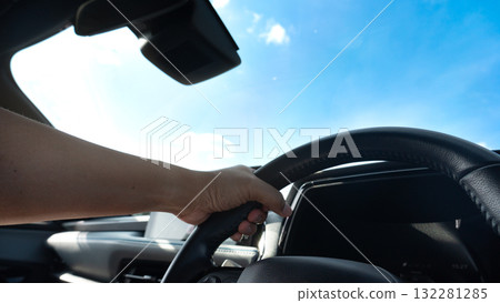 Hand on steering wheel of car on blue sky and white clouds background. Single hand control steering wheel. Driving for travelling to the nature. 132281285