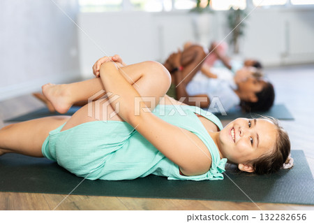 Girls and boys doing abdominal crunches with outstretched arms to strengthen abs and core muscles during group yoga class in studio Girls and boys doing abdominal crunches with outstretched arms to strengthen abs and core muscles during group yoga class in studio 132282656