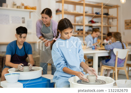 Children working at potter's wheel with teacher in art studio 132282670