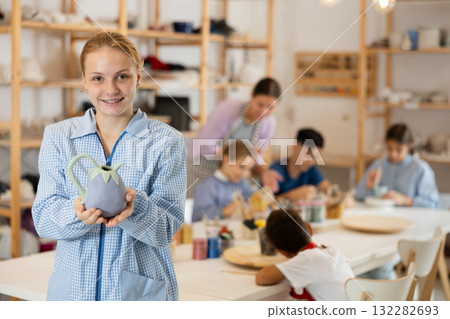 Girl holds a clay product against the background of students and a teacher Girl holds a clay product against the background of students and a teacher 132282693