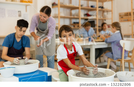 Children working at potter's wheel with teacher in art studio Children working at potter's wheel with teacher in art studio 132282806