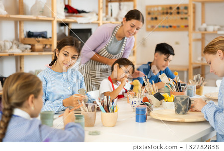 Children painting ceramics with a teacher 132282838