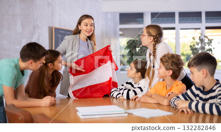 Positive female teacher discussing with preteens students state flag of Austria in auditory of middle school 132282846
