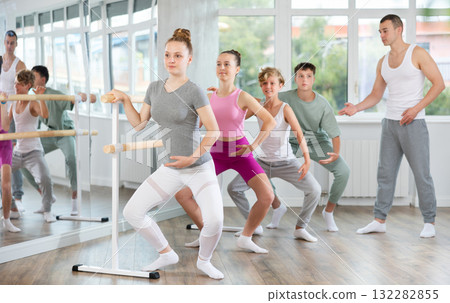 Teenagers doing ballet at group training session in the studio performs demi plie near the ballet barre, standing in ballet stance 132282855